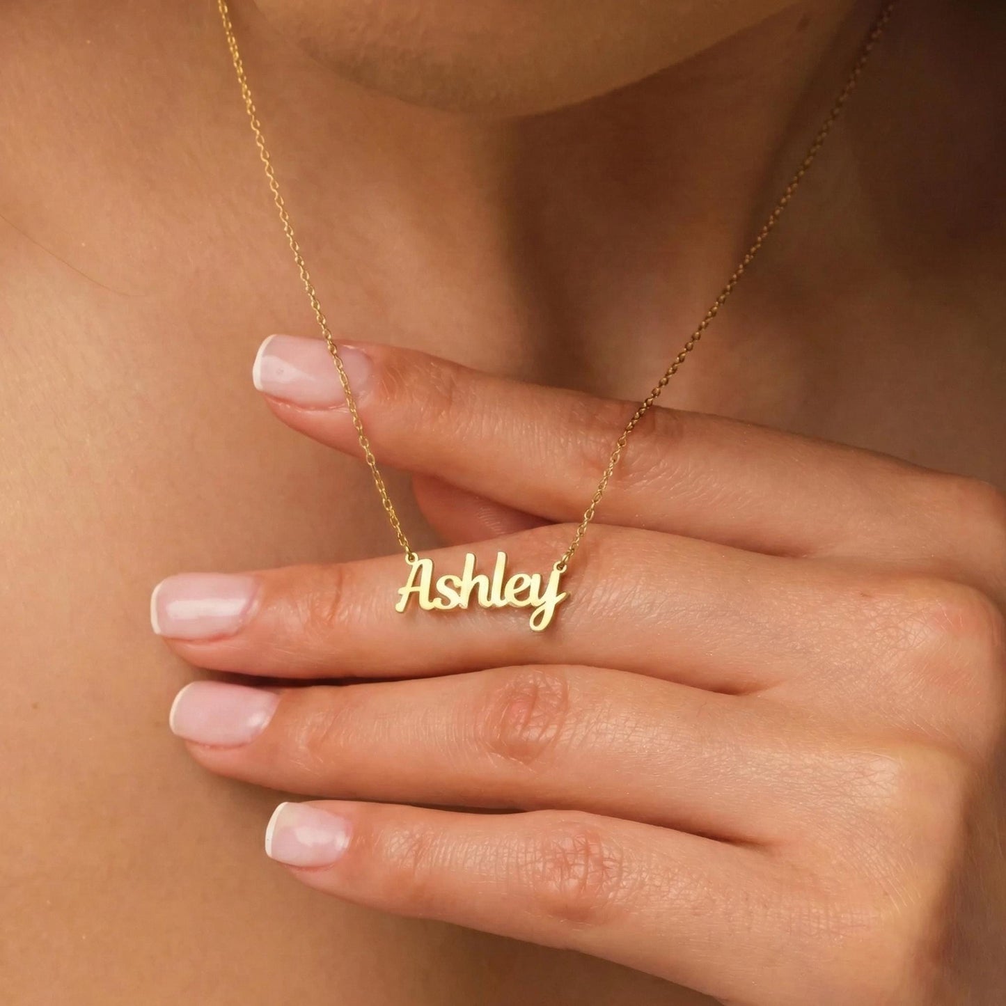 May include: A gold-colored necklace with the name "Ashley" in a cursive font. The necklace is on a delicate chain. The name is the focal point, and the necklace is displayed on a person's skin.