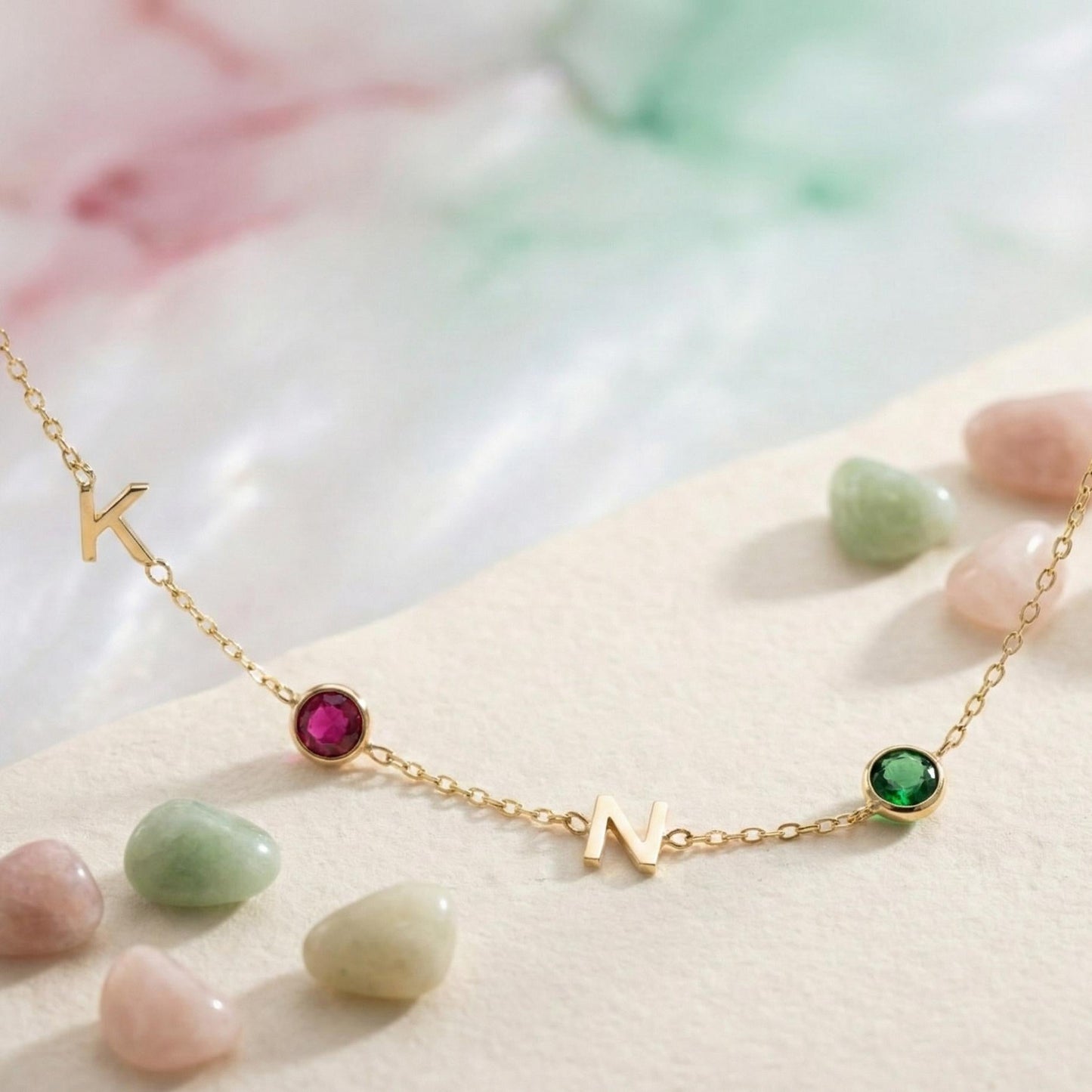 Dainty gold necklace featuring sideways initials and bezel set birthstones, personalized family jewelry for mother's day gift, minimalist custom letter necklace with ruby and emerald colored stones on neck.