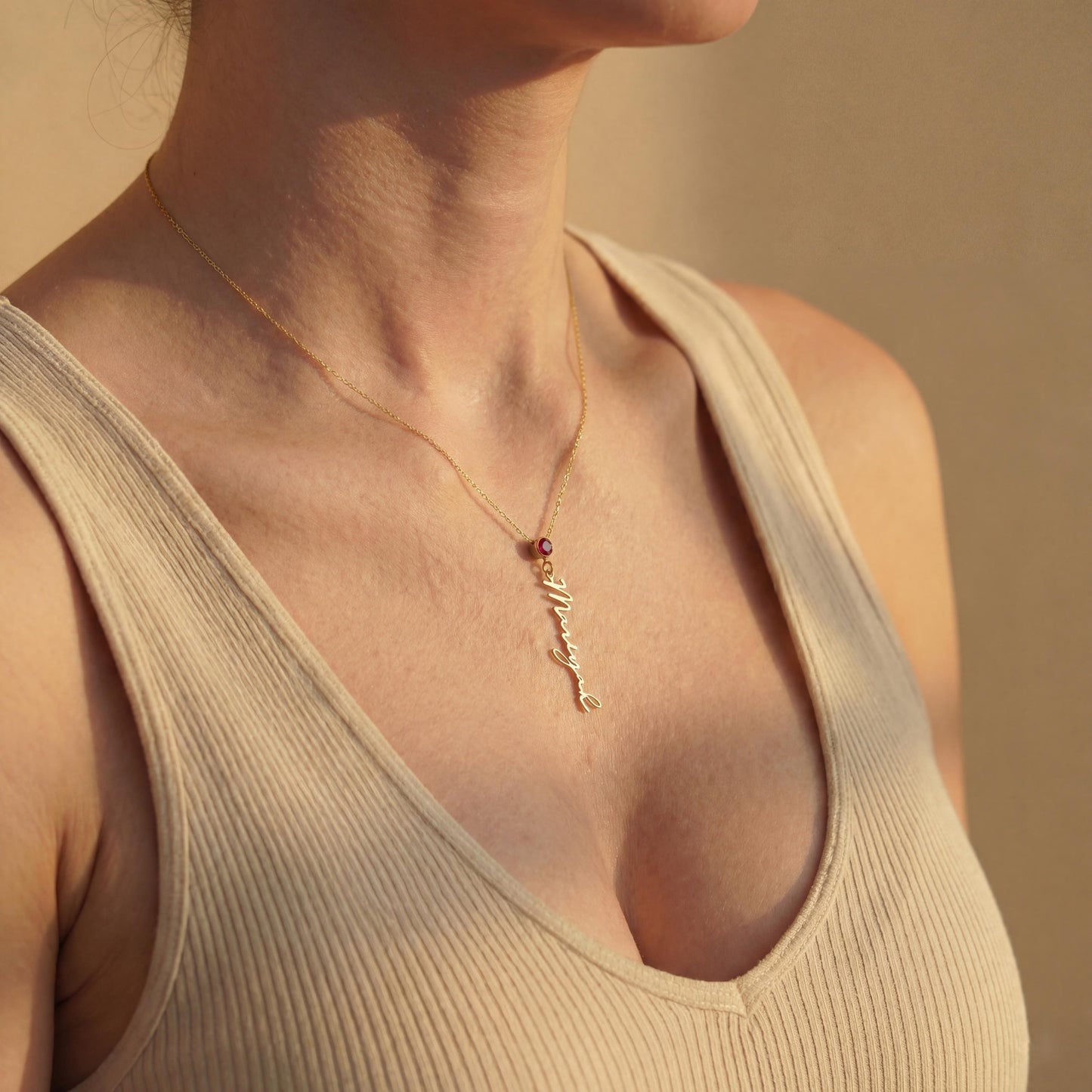Vertical name necklace with round red garnet birthstone, gold custom script nameplate pendant on model, personalized mothers day gift for women