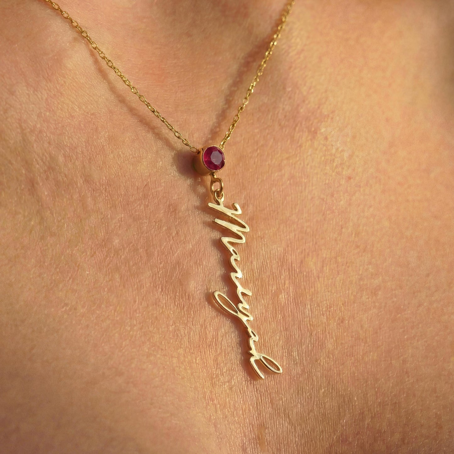 Vertical name necklace with round red garnet birthstone, gold custom script nameplate pendant on model, personalized mothers day gift for women