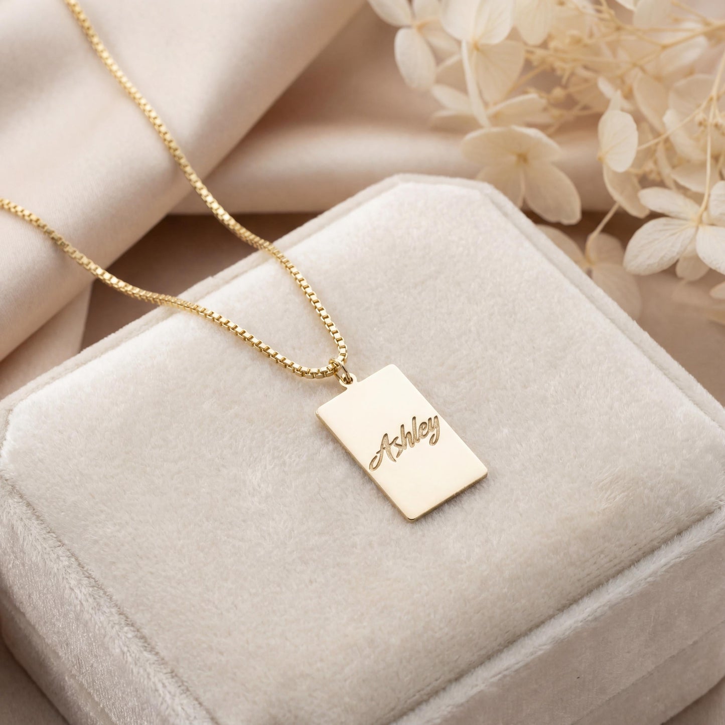 Gold vertical bar necklace on a model's neck, personalized with the engraved name Ashley in cursive font. Minimalist rectangular pendant gift for mother's day.