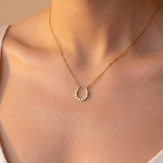Dainty 14K gold horseshoe necklace worn delicately on a woman's neck, minimalist lucky charm pendant jewelry ideal for everyday wear and thoughtful Mother's day gift.