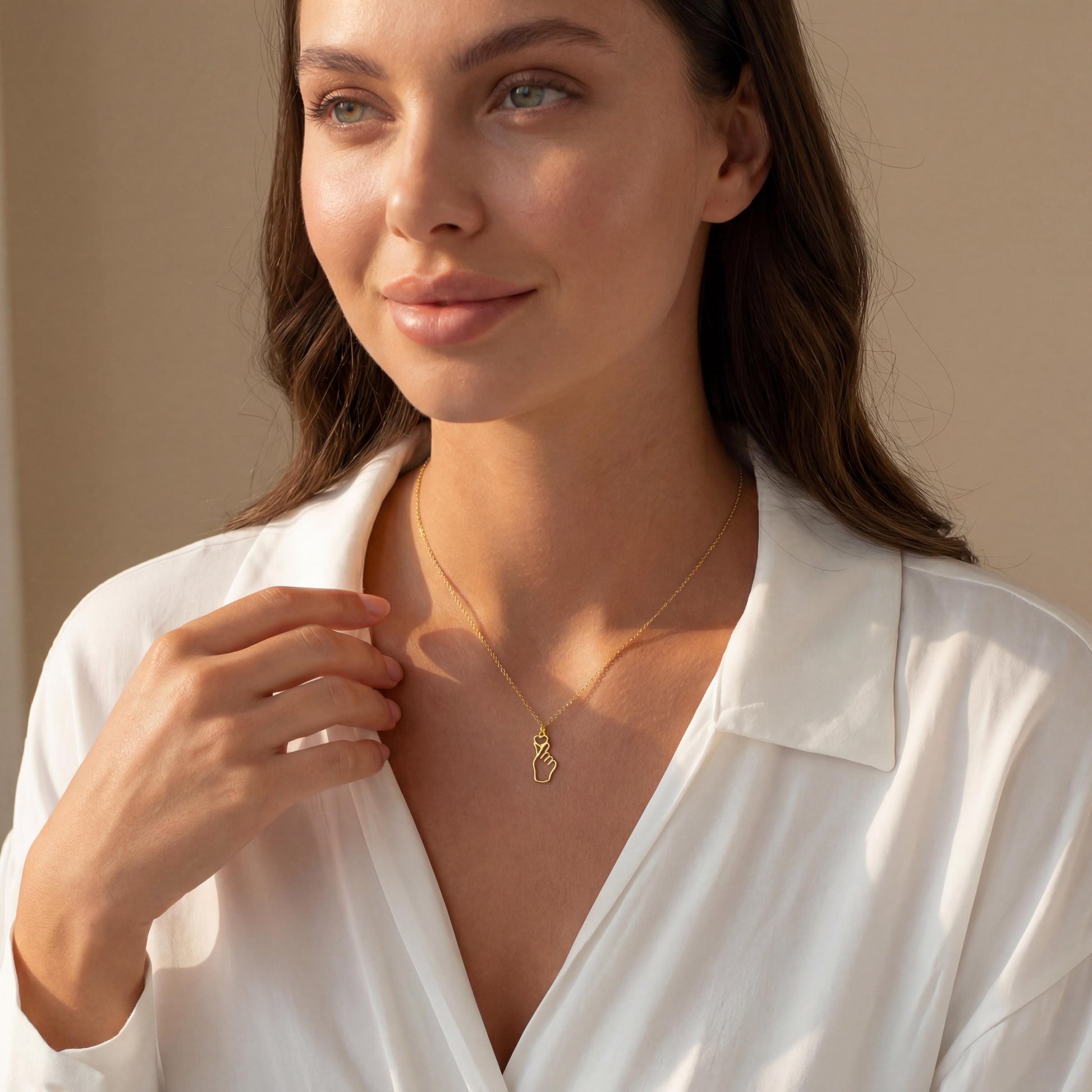 A woman wearing a dainty 14K gold minimalist Korean finger heart necklace, a delicate saranghae hand gesture pendant resting on her collarbone.