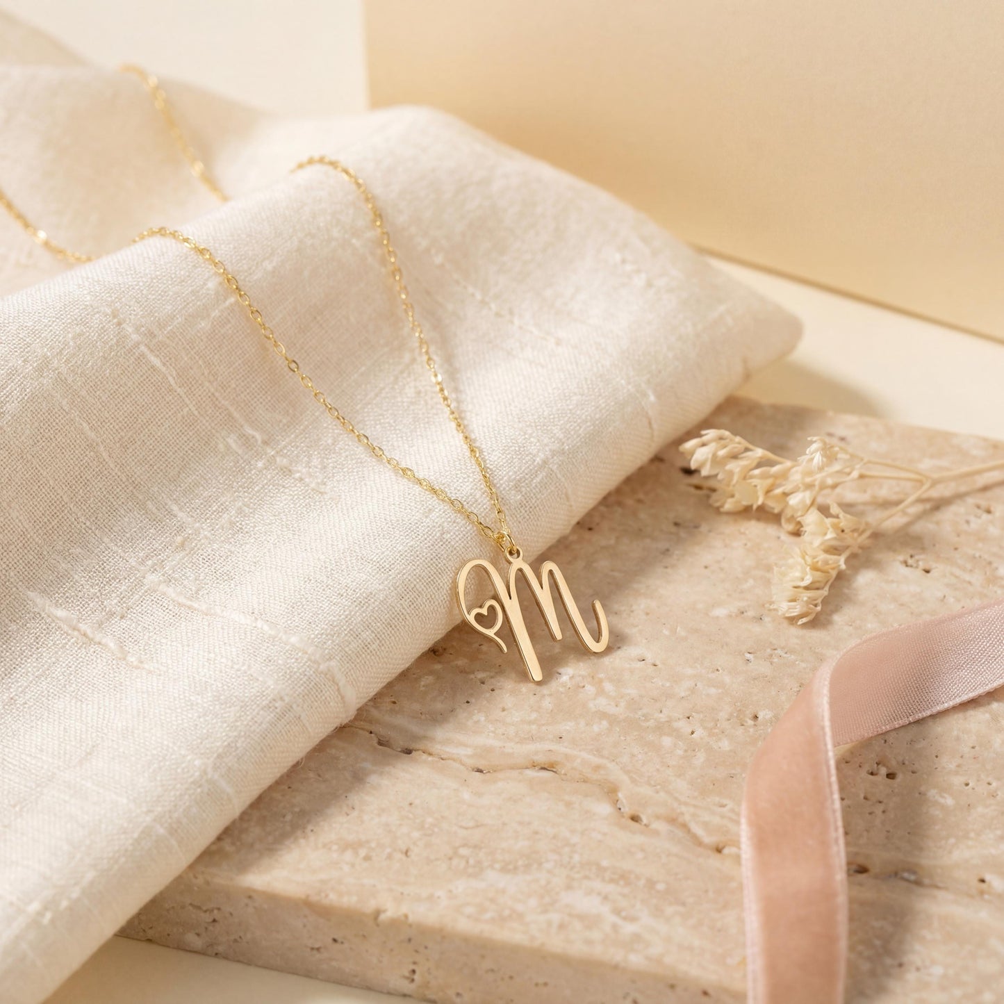 Dainty custom initial necklace with a delicate heart detail next to a cursive letter M, worn by a smiling woman in sunlight. Minimalist personalized elegant pendant.