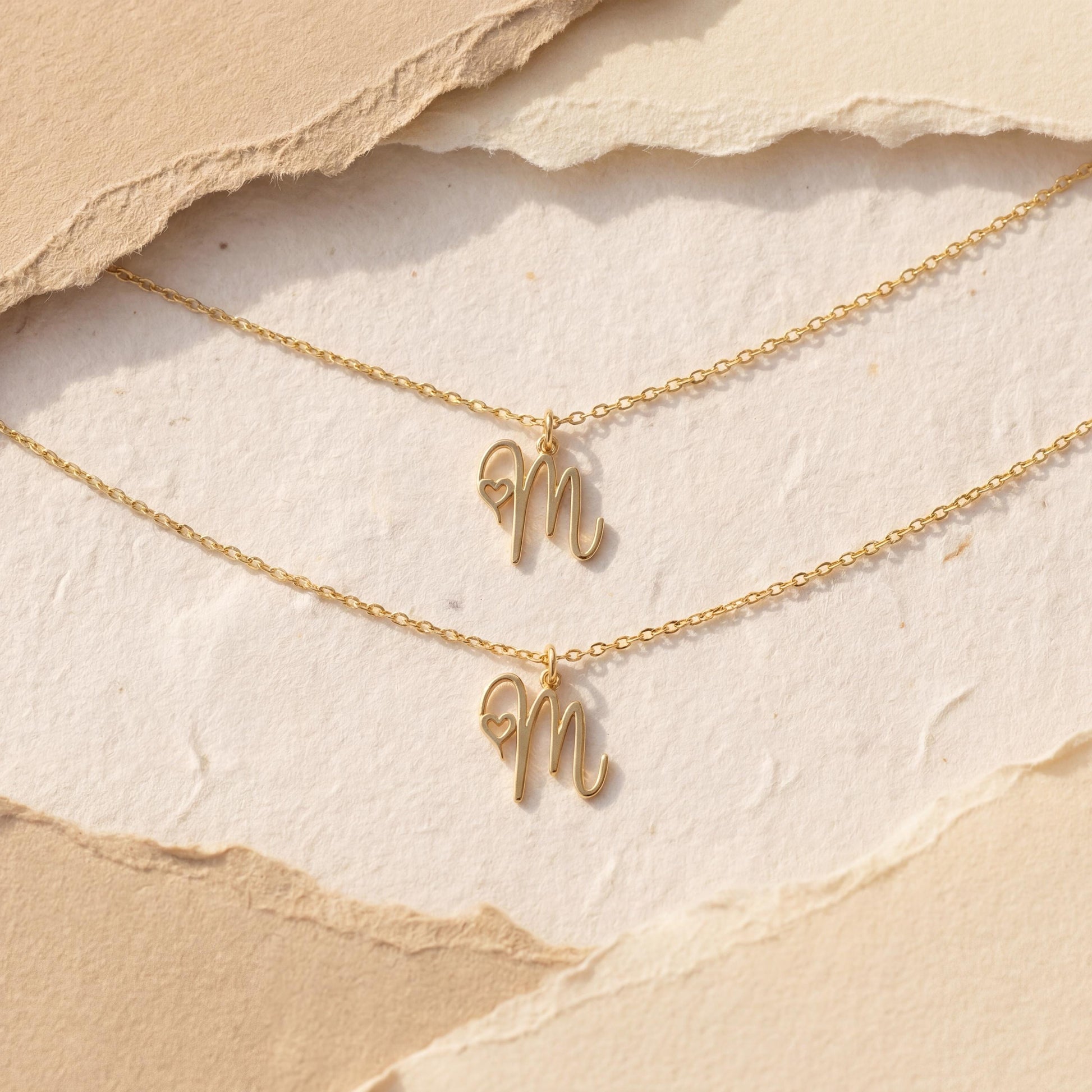Dainty custom initial necklace with a delicate heart detail next to a cursive letter M, worn by a smiling woman in sunlight. Minimalist personalized elegant pendant.
