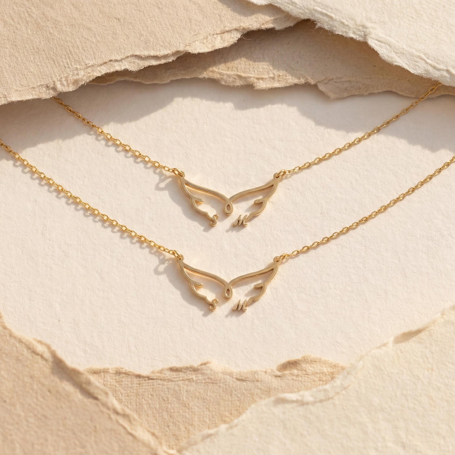 Dainty custom angel wing necklace featuring two personalized initial letters nesting at the bottom of the wings, worn on a woman's collarbone during golden hour.
