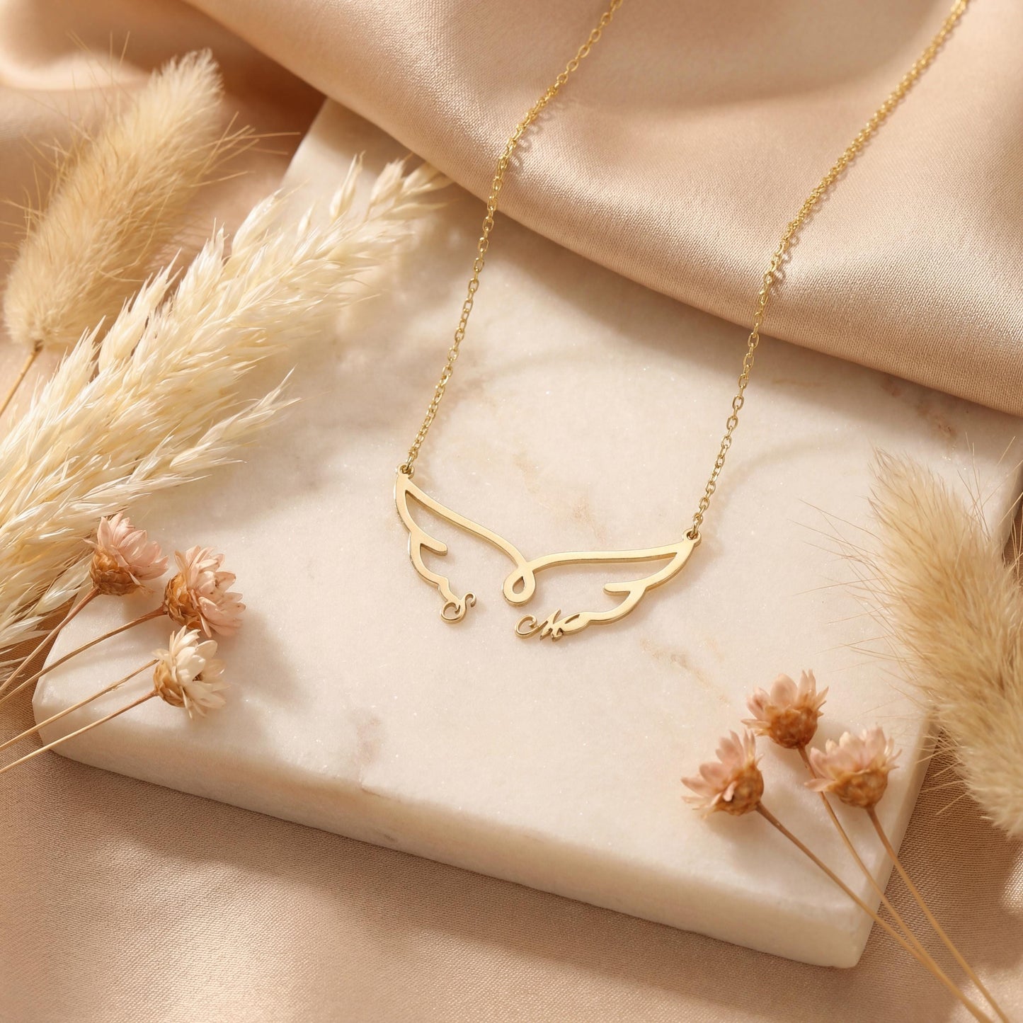 Dainty custom angel wing necklace featuring two personalized initial letters nesting at the bottom of the wings, worn on a woman's collarbone during golden hour.