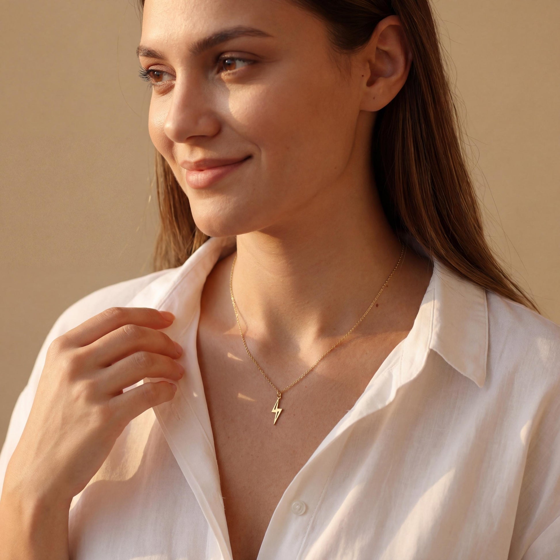 Close-up of a delicate minimalist 14k gold plated lightning bolt pendant necklace worn by a woman in a white shirt, glowing in soft sunlight.