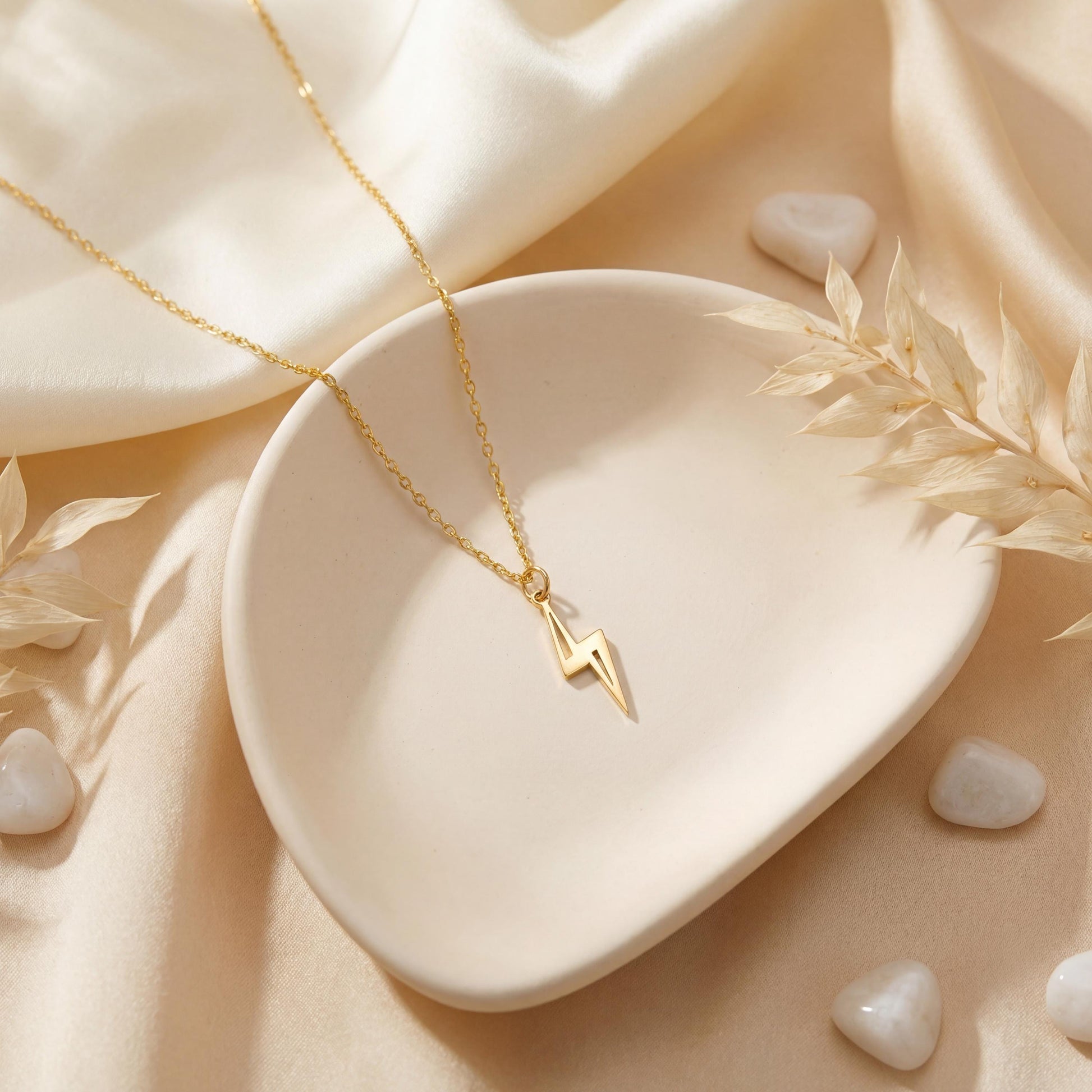Close-up of a delicate minimalist 14k gold plated lightning bolt pendant necklace worn by a woman in a white shirt, glowing in soft sunlight.