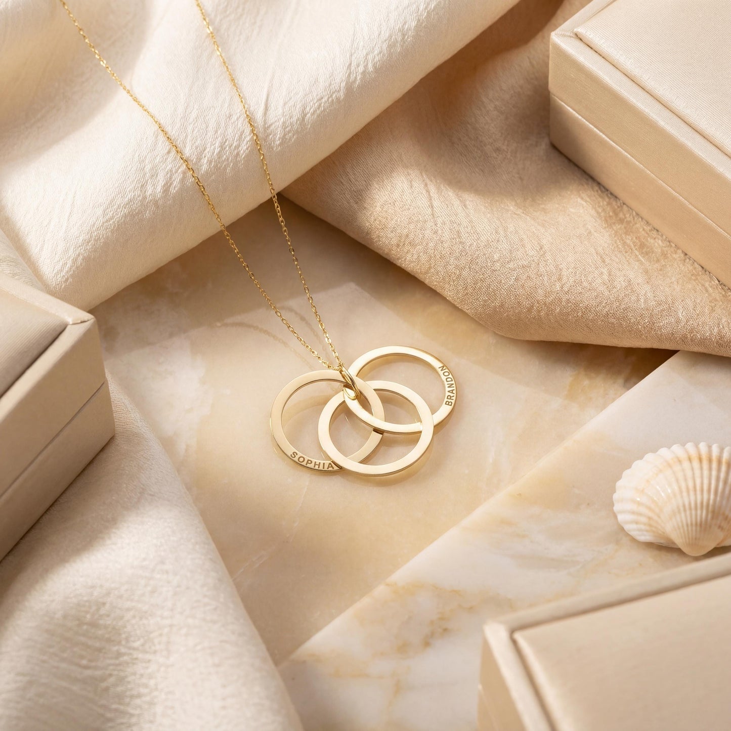 14K gold plated interlocking circle necklace featuring three beautifully intertwined rings, delicately custom engraved with the family names Sophia and Brandon, resting elegantly on a woman's collarbone.