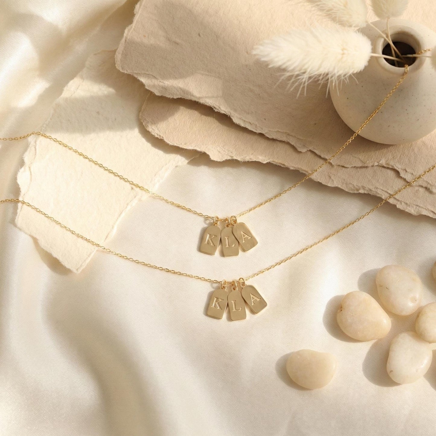 Gold initial necklace featuring three small rectangular pendant tags engraved with letters K L A, worn on a woman's neck, minimalist personalized jewelry for mom