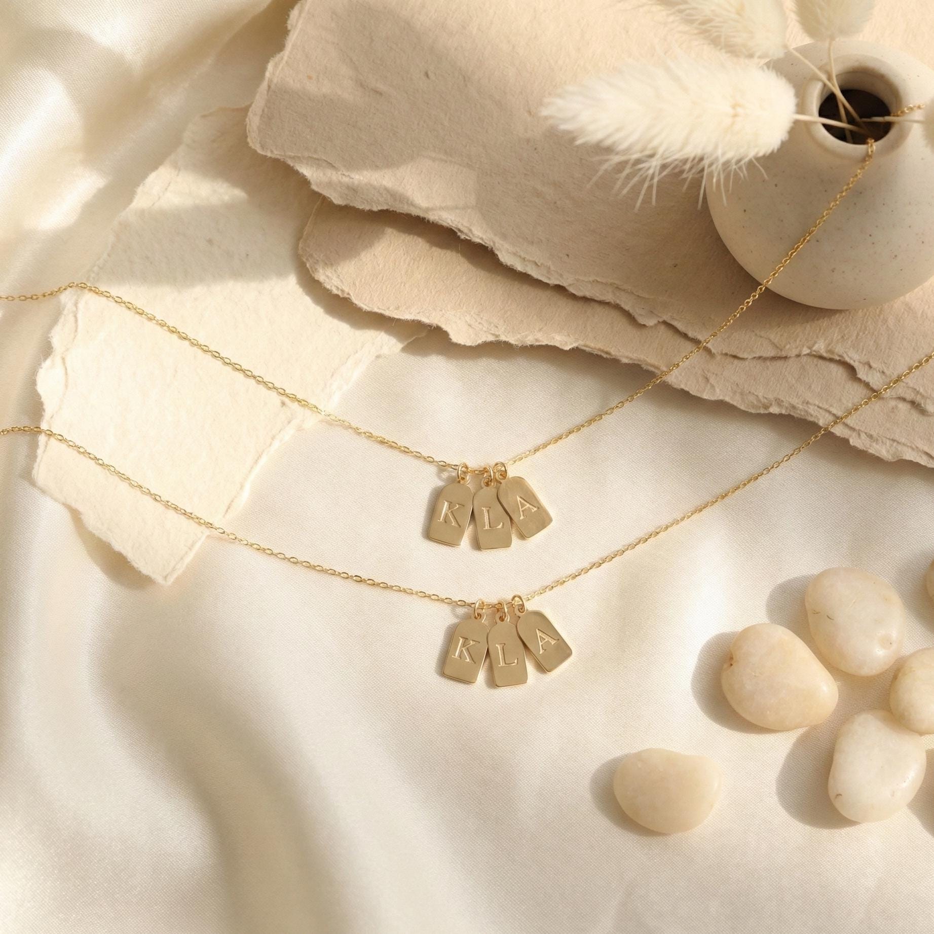 Gold initial necklace featuring three small rectangular pendant tags engraved with letters K L A, worn on a woman's neck, minimalist personalized jewelry for mom