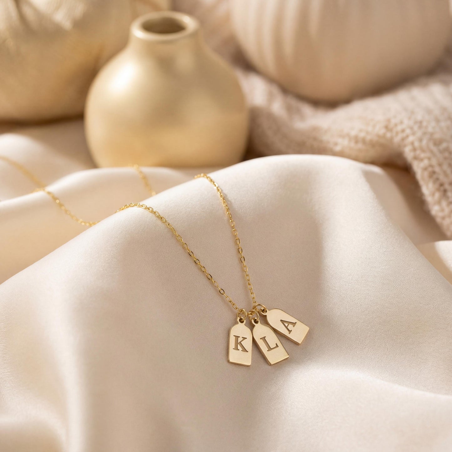 Gold initial necklace featuring three small rectangular pendant tags engraved with letters K L A, worn on a woman's neck, minimalist personalized jewelry for mom