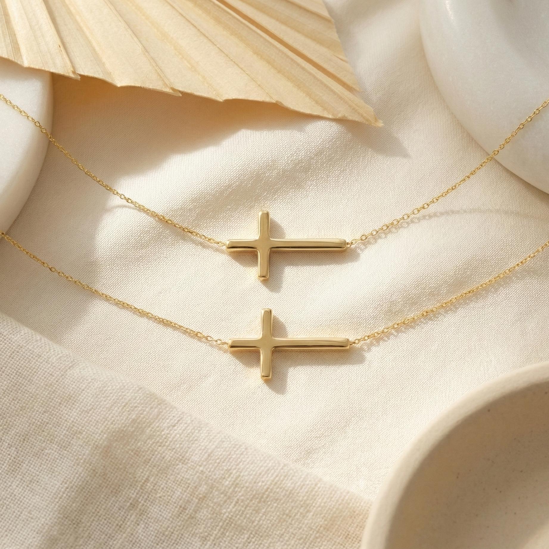 Close up of gold sideways cross pendant, delicate chain jewelry for layering, modern faith necklace flat lay
