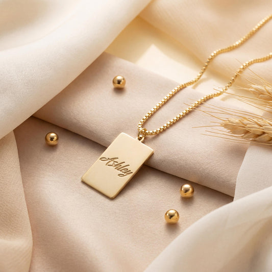 Gold vertical bar necklace on a model's neck, personalized with the engraved name Ashley in cursive font. Minimalist rectangular pendant gift for mother's day.