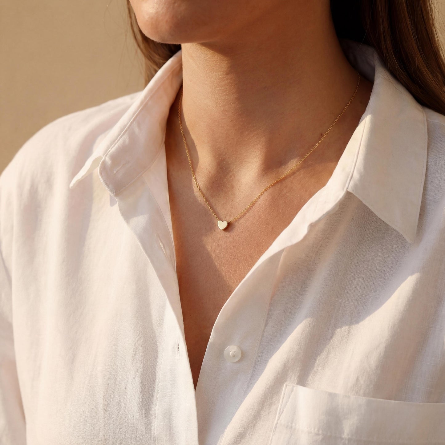 Minimalist 14k gold plated tiny puff heart necklace on a model wearing a white shirt, dainty gold choker chain detail, small heart pendant close up, perfect mothers day gift or birthday jewelry for her.