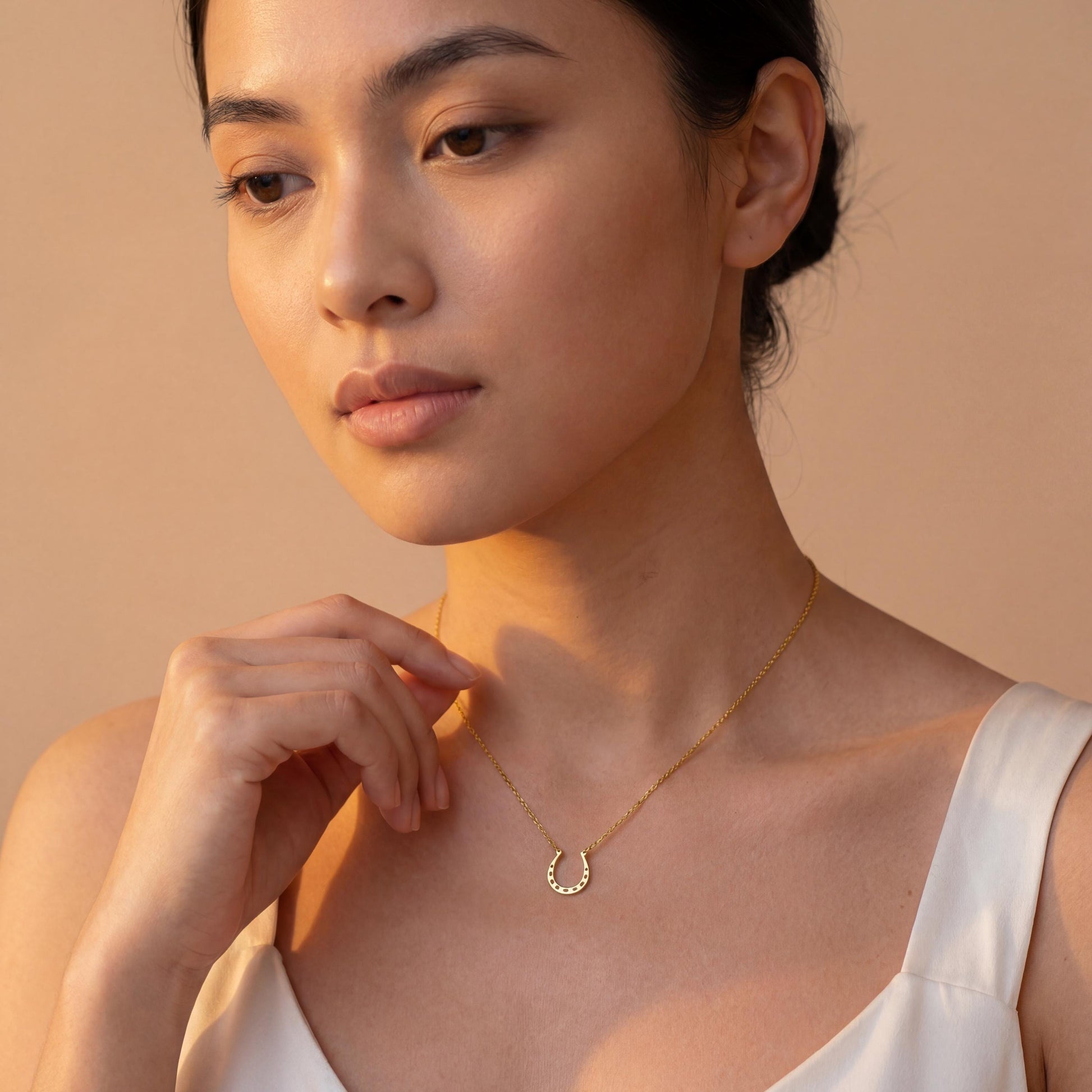Dainty 14K gold horseshoe necklace worn delicately on a woman's neck, minimalist lucky charm pendant jewelry ideal for everyday wear and thoughtful Mother's day gift.