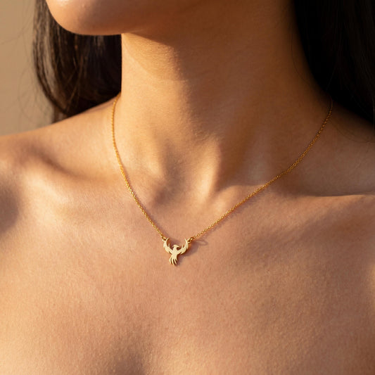 Minimalist gold phoenix pendant necklace worn on a woman's collarbone in warm sunlight, symbolizing rebirth and strength, ideal for Mothers Day gifting